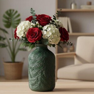 May include: A dark green ceramic vase with a textured, embossed fern leaf pattern on its exterior. The vase holds a floral arrangement consisting of deep red roses, white hydrangea clusters, small white berries, and green eucalyptus sprigs.