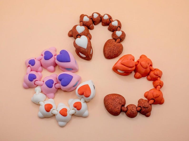 May include: An assortment of decorative heart and bear-shaped embellishments in various colors. The collection includes pink, white, and brown pieces, each with contrasting heart accents in purple, red, and white. These are likely for crafting or jewelry making.