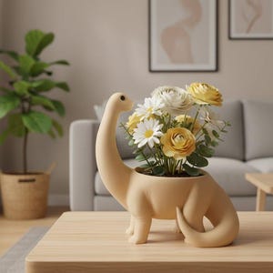 May include: A matte beige ceramic planter shaped like a long-necked dinosaur, filled with a bouquet of white and yellow flowers with green leaves. The dinosaur figure has a smooth, rounded body, a curved neck, and a curled tail, serving as a vessel.