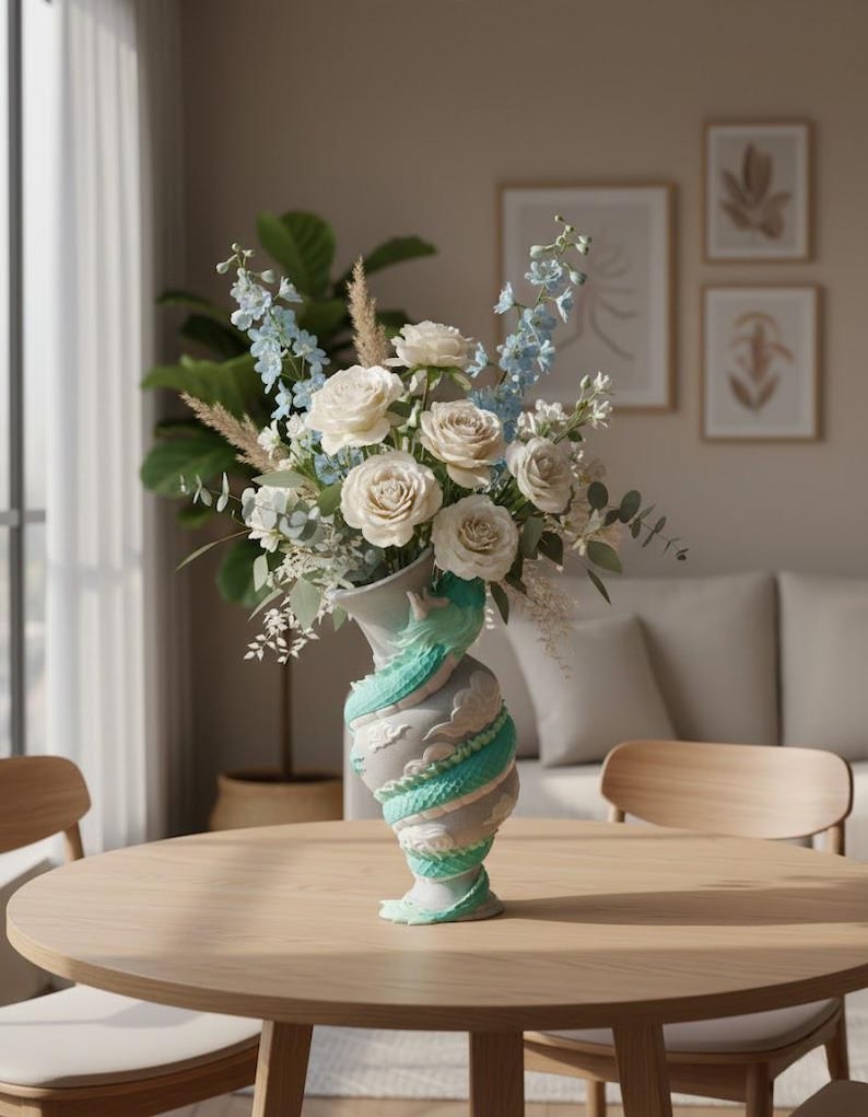 May include: A light gray vase featuring a sculpted teal dragon wrapping around its body, filled with a floral arrangement of white roses, light blue delphinium stalks, pampas grass, and green eucalyptus leaves.