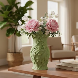 May include: A matte sage green ceramic vase featuring a raised, swirling vine and leaf relief pattern. The vase is filled with a bouquet of large, soft pink peony flowers and delicate white sweet pea blossoms with green stems and foliage.