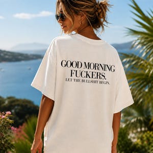 Könnte beinhalten: Ein cremefarbenes T-Shirt mit kurzen Ärmeln und schwarzem Text auf der Rückseite, der lautet: GOOD MORNING FUCKERS. LET THE BULLSHIT BEGIN. Das Shirt hat eine lockere Passform mit Rundhalsausschnitt und besteht aus einem blickdichten Stoff.