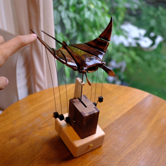 A hand-carved walnut-toned manta ray that actually 'flies' through mechanical automata motion — the kind of desk sculpture that stops conversations cold.