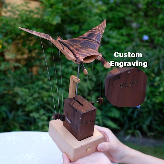 A hand-cranked wooden automaton where a manta ray actually flaps and 'flies' through the air — pure kinetic magic carved from wood.