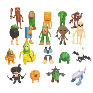 May include: A collection of colorful, whimsical figurines, each with a unique design. The figures include a brown figure with a bat, a cactus-like figure, a monkey in a banana, and a shark with blue shoes. The toys are made of plastic.