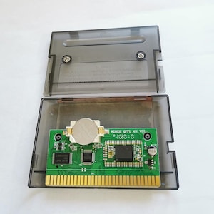 Op de afbeelding: Een heldere, open, rechthoekige cartridgebehuizing met een groene printplaat erin. De printplaat heeft goudkleurige pinnen, een zilveren batterij en zwarte chips. De tekst "WDI802_QPPL_4M_V03" en "2020:10" is op de printplaat gedrukt.