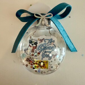 May include: Clear glass Christmas ornament with a teal ribbon bow. Inside the ornament are confetti, a sticker of a polar bear wearing sunglasses and a scarf, and the text "The Summer I turned Pretty".