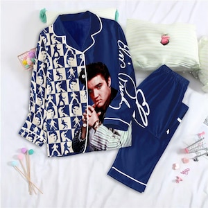 May include: Navy blue pyjama set featuring a portrait of Elvis Presley and a checkered pattern of Elvis silhouettes. The set includes a button-down top with white piping and matching trousers. The words "Elvis Presley" are written in white script on the top.