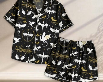 以下が含まれることがあります： 黒の半袖ボタンダウンシャツとショートパンツのセット。白と金のドラゴン、剣、星の模様が繰り返されています。シャツにはノッチドラペルと白いパイピングが施されています。生地には「Wing leader」および「Fourth Wing」という文字がプリントされています。