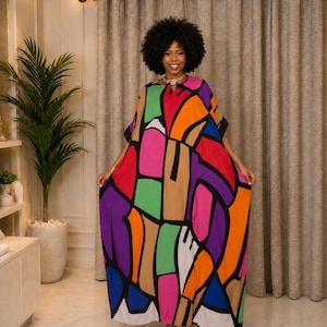 Op de afbeelding: Een vloerlange kaftan-jurk met een gedurfd, abstract geometrisch patroon met grote, onregelmatige vormen in levendige tinten oranje, paars, roze, groen, blauw en beige, omlijnd door dikke zwarte lijnen met een eenvoudige ronde halslijn.