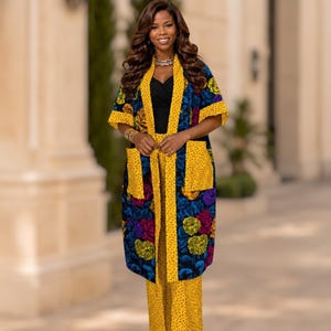 May include: A long, open-front kimono-style jacket featuring a dark blue base with vibrant floral patterns in yellow, purple, and green, paired with matching yellow wide-leg trousers that have a small black dash print throughout the fabric.