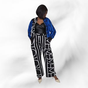 May include: A black and white patterned wide-leg trouser suit with a blue and black bomber jacket. The trousers have a vertical stripe design with white lettering. The jacket has blue and black striped sleeves. The outfit is paired with cream-coloured heels.