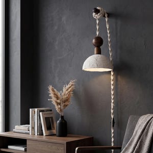 May include: A wall-mounted lamp with a textured, off-white shade and a dark wooden accent. The lamp hangs from a thick, twisted rope. The design includes a dark wooden base and a black switch. The lamp is part of a home decor theme.