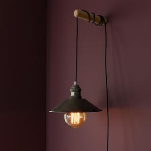 May include: A hanging pendant light with a dark metal shade and a visible Edison-style bulb. The light is suspended from a wooden dowel attached to the wall with a black cord. The background is a deep burgundy color.
