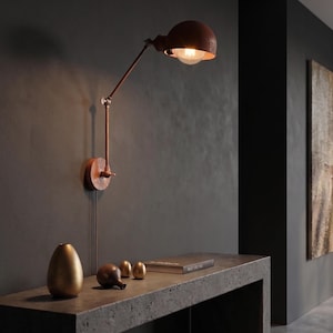 May include: A wall-mounted lamp with a copper-toned finish, featuring an adjustable articulated arm and a dome-shaped shade. The lamp emits a warm glow from an exposed light bulb, providing focused illumination directed downward from the fixture.