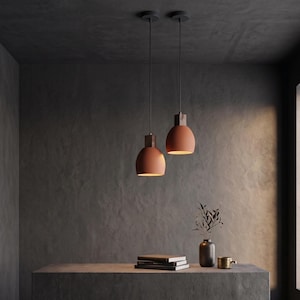 May include: Two terracotta-colored dome pendant lights with dark wooden top accents hang from thin black cords. The lights feature a smooth finish and emit a warm glow from the bottom opening, illuminating the space below them in a soft light.