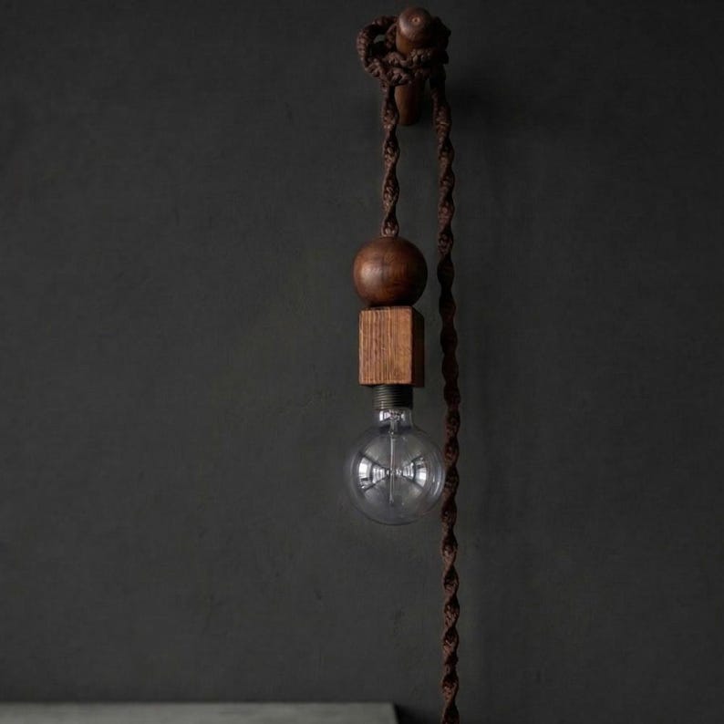 Peut inclure: Suspension luminaire moderne et artisanal. Le design comprend une sph&egrave;re et un cube en bois, une ampoule transparente et un cordon torsad&eacute; marron. La lampe est suspendue &agrave; un support mural en bois, cr&eacute;ant une ambiance chaleureuse.