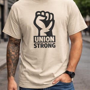 May include: Beige t-shirt with a black graphic of a clenched fist and the words "UNION STRONG" in a bold, sans-serif font. The shirt is made of a soft material and is suitable for casual wear.