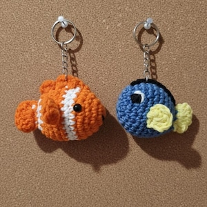 Può includere: Due portachiavi a forma di pesce all'uncinetto. Uno è arancione con strisce bianche, l'altro è blu con pinne gialle. Entrambi hanno occhi neri e portachiavi argentati attaccati con catene. Fatto a mano.