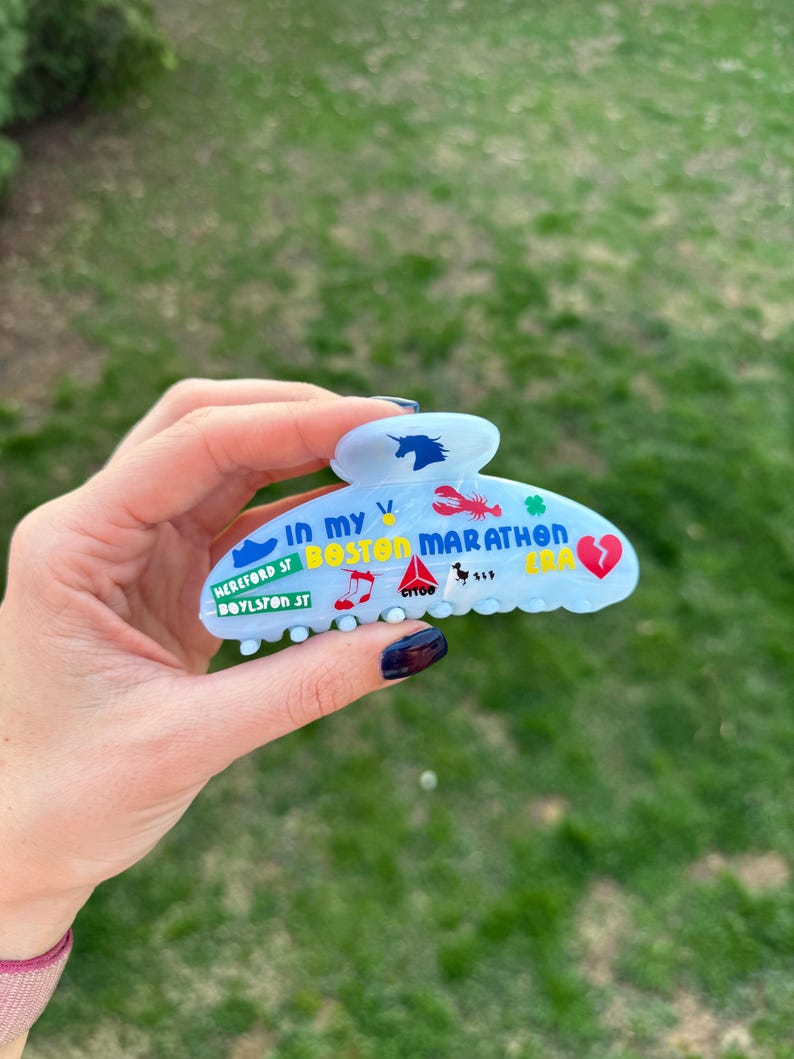 May include: A pale blue hair claw clip decorated with colourful graphics and text, including a unicorn, lobster, and the words "Boston Marathon." The clip also features the text "Hereford St, Boylston St."
