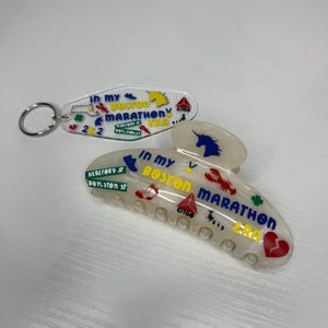 May include: A clear acrylic keychain and hair clip with the text "In My Boston Marathon Era". The keychain has a horse graphic, and the hair clip features a unicorn, lobster, and heart. The clip also has the text "Hereford St, Boylston St".