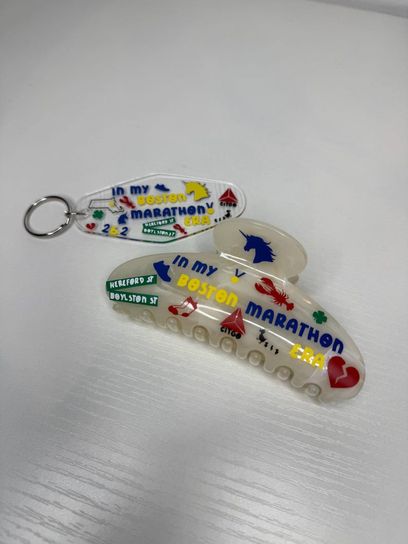 May include: A clear acrylic keychain and hair clip with the text "In My Boston Marathon Era". The keychain has a horse graphic, and the hair clip features a unicorn, lobster, and heart. The clip also has the text "Hereford St, Boylston St".