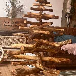 Pode incluir: Escultura artesanal de árvore de Natal em madeira, feita com ramos e troncos. A árvore tem um aspeto natural e rústico. É exibida num terraço de madeira. Um objeto decorativo único.