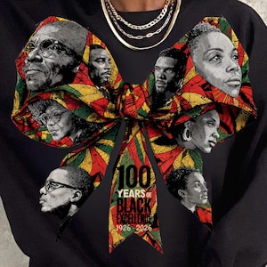 May include: Black sweatshirt with a bow design featuring portraits of Black figures. The bow is decorated with red, yellow, and green patterns. The text "100 Years of Black Excellence 1926-2026" is printed on the bow.