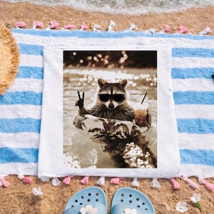 Può includere: Immagine in seppia di un procione con occhiali da sole che galleggia in una piscina su un telo da mare. Il procione è in un anello gonfiabile e tiene in mano una bevanda. L'asciugamano è bianco con strisce blu e nappe.