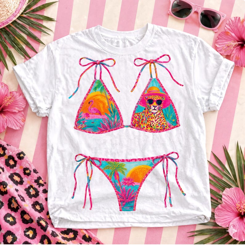 May include: White t-shirt with a colorful bikini design. The bikini top features a flamingo and a leopard wearing sunglasses. The bikini bottom has a tropical sunset design. Pink and blue accents are used throughout the design.