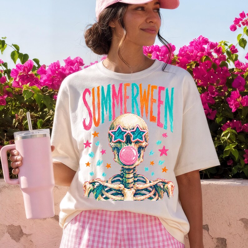 May include: Cream-colored t-shirt with the word "SUMMERWEEN" in colorful letters. The shirt features a skeleton wearing star-shaped sunglasses and blowing a bubblegum bubble. Pink and blue stars surround the skeleton.