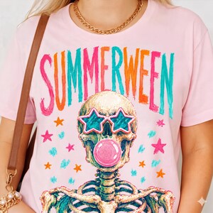 May include: Pink t-shirt with the word "SUMMERWEEN" in colorful letters. The graphic features a skeleton wearing star-shaped sunglasses and blowing a bubble. Pink, orange, teal, and gold stars are scattered around the skeleton.