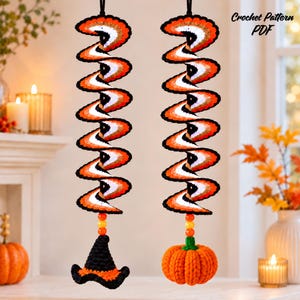May include: Two hanging crochet spiral decorations featuring orange, white, and black stripes. One spiral ends with a black witch hat, the other with an orange pumpkin. Each has a black hanging loop and colourful beads. Text reads Crochet Pattern PDF.