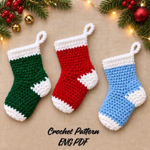 May include: Three small crocheted stockings in green, red, and light blue, each featuring a white cuff, heel, and toe. The text Crochet Pattern ENG PDF is printed in black at the bottom center of the image.