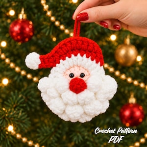 May include: A crocheted Santa Claus ornament featuring a red hat with a white pom-pom, a peach-coloured face, black bead eyes, a red nose, and a thick white beard. The ornament includes a small red loop at the top for hanging on a tree.