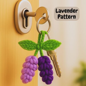 May include: A handmade key chain with a lavender pattern. The key chain features a green stem and leaves, with two clusters of lavender-colored flowers. The key chain is attached to a key ring with a gold-coloured key.