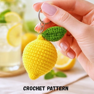Peut inclure: Un porte-clés en forme de citron crocheté, avec une feuille verte et un anneau argenté. Le citron est jaune vif et a une surface texturée. Les mots "CROCHET PATTERN" sont imprimés en noir en bas de l'image.
