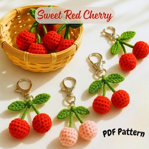 May include: Crocheted cherry keychains and cherries in a basket. The keychains feature red and pink cherries with green leaves and silver clasps. The text "Sweet Red Cherry" and "PDF Pattern" are visible.