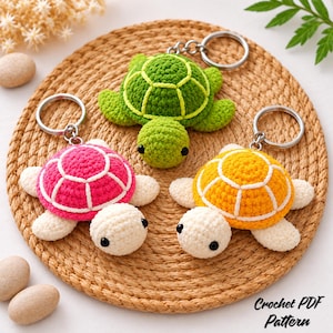 Può includere: Tre portachiavi a forma di tartaruga all'uncinetto con gusci verde, rosa e giallo con cuciture bianche. Ogni tartaruga ha testa e pinne color crema, occhi a perla neri e un anello portachiavi in metallo argentato. Testo: Crochet PDF Pattern.