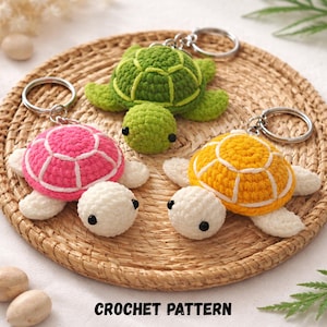 May include: Three crocheted turtle keyrings in pink, green, and yellow, each with a white belly and flippers. The turtles have black eyes and silver key rings. The keyrings are displayed on a woven, circular mat. The text "CROCHET PATTERN" is at the bottom.