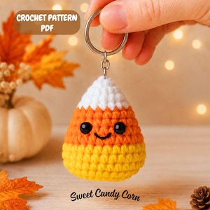 May include: A crochet candy corn keychain featuring a white top, orange middle, and yellow bottom section with black safety eyes and a stitched smile. The keychain includes a metal ring and is labeled with the text CROCHET PATTERN PDF and Sweet Candy Corn.