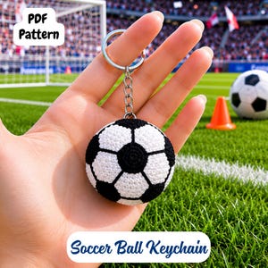 May include: A crocheted soccer ball keychain featuring a classic black and white pentagonal pattern. The spherical charm is attached to a silver-toned metal split ring by a short chain. The text PDF Pattern and Soccer Ball Keychain are visible.