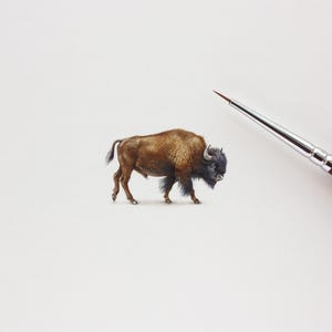May include: A watercolour painting of a bison, in shades of brown and black, with a brush in the upper right corner. The bison is depicted walking, showing its shaggy fur and horns. The artwork is on a white background.