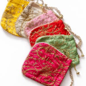 May include: Six embroidered drawstring pouches in a range of colours: yellow, beige, pink, red, green, and fuchsia. Each pouch has gold embroidery and a beaded chain strap. The pouches are arranged diagonally, with a white background.