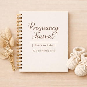 May include: A cream-colored pregnancy journal with gold spiral binding, featuring the text "Pregnancy Journal | Bump to Baby | 40 Week Memory Book." The image includes a pair of baby booties and dried flowers.
