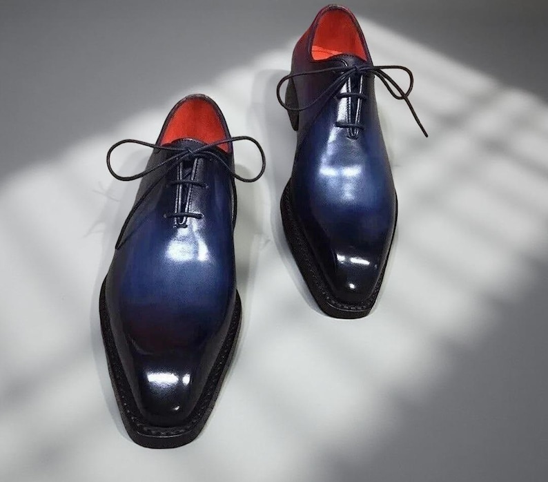 May include: A pair of men's dress shoes with a gradient blue and black finish. The shoes have a pointed toe, a lace-up closure, and a red interior. The shoes are made of a glossy material.