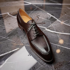 Peut inclure: Une chaussure de ville en cuir marron avec une tige texturée et un bout verni. La chaussure est dotée de lacets gris foncé et d'un petit talon. L'intérieur est de couleur beige clair. La chaussure est conçue pour les occasions formelles.