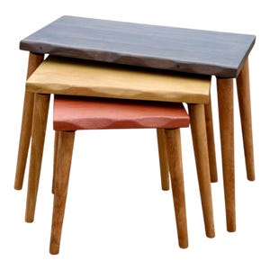 Pode incluir: Conjunto de três mesas de encaixe com pernas de madeira e tampos retangulares. Os tampos são em tons de cinza, amarelo e vermelho. As mesas são projetadas para empilhar para economizar espaço. Cada mesa tem uma borda natural única.