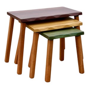 Può includere: Un set di tre tavolini ad incastro in legno di diverse dimensioni. I piani sono tinti nei toni del marrone, giallo e verde. Le gambe sono in legno naturale. I tavoli hanno un design semplice e moderno, adatti a vari usi.