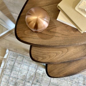 Può includere: Un oggetto sferico color rame è appoggiato su un tavolo di legno a tre livelli. Il tavolo ha un bordo marrone scuro e una finitura a venature naturali. Sul tavolo ci sono anche libri e una piccola casa decorativa bianca.